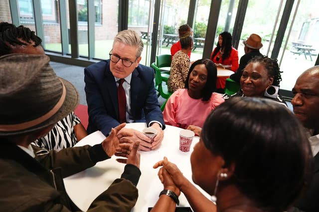 Sir Keir Starmer sits at a table drinking coffee with members of the Windrush generation