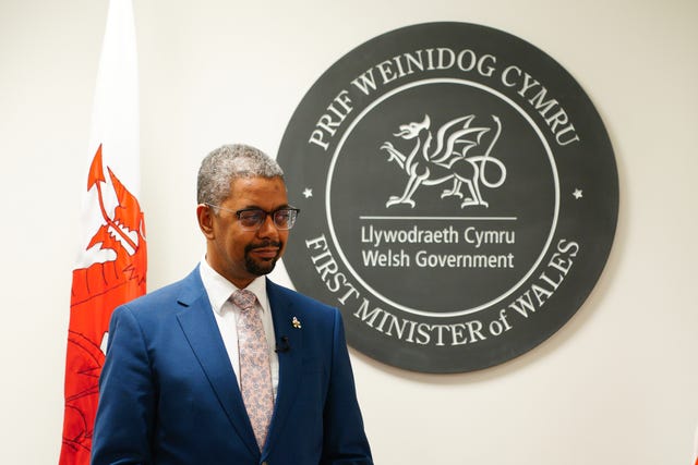 Vaughan Gething next to a Welsh flag and a sign reading 'First Minister of Wales'