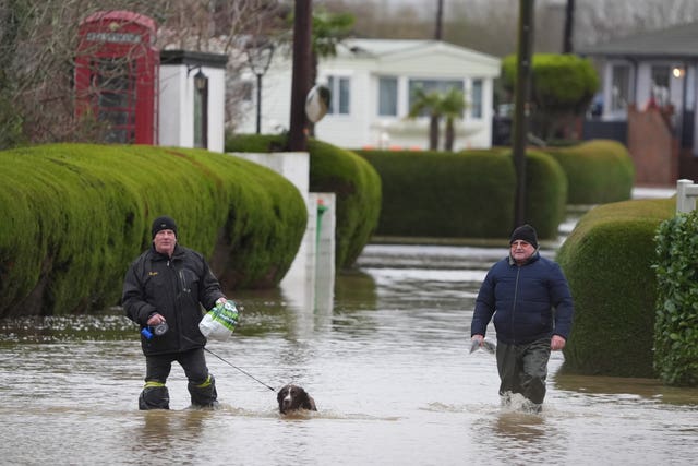 Men and a dog walk through flood water at the Little Venice caravan park in Yalding Kent