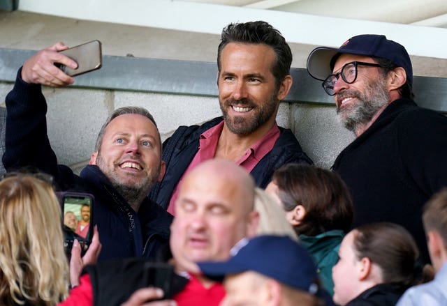 Co-owner Ryan Reynolds (centre) and Hugh Jackman (right) pose for a photo with a fan as Wrexgham marked their return to the Football League with a 5-3 home defeat by MK Dons