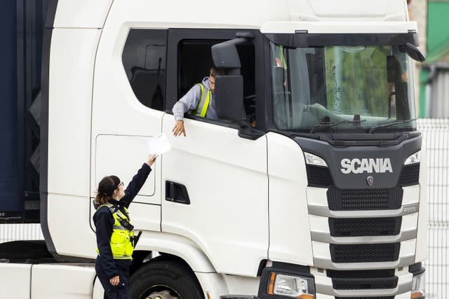 A person in a hi-vis vest hands a piece of paper to the driver of a white wagon