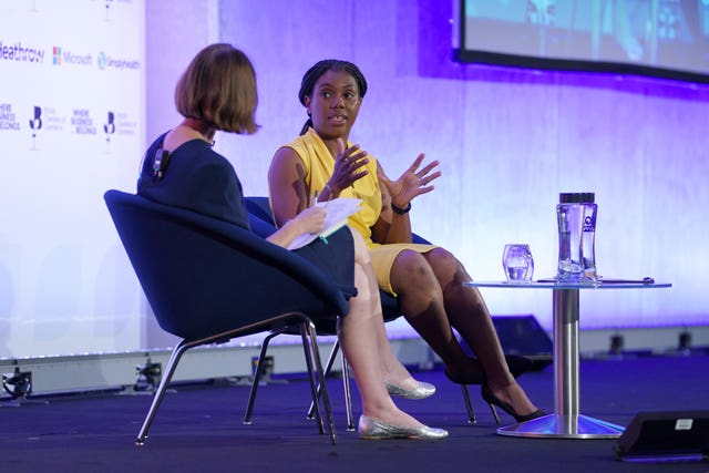 Kemi Badenoch turned slightly towards the camera speaks to a compere as part of a Q&A session in a hall, lit up in purple 