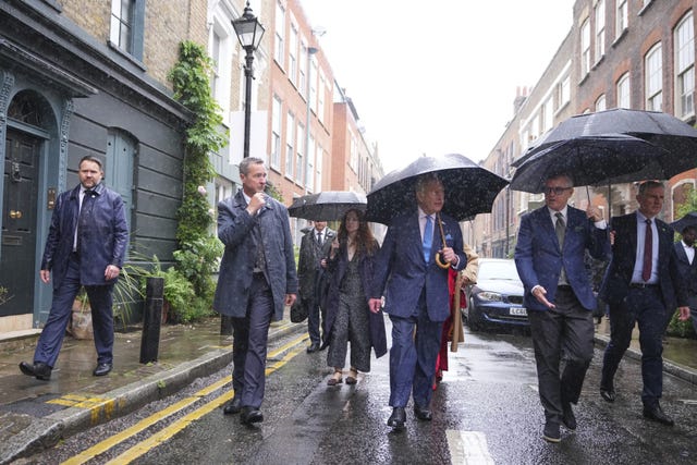 The King and a group of people in the rain with umbrellas