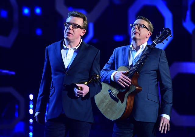 The Proclaimers standing on stage, one holding a guitar and the other holding an award