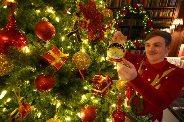 A worker adds a decoration featuring an image of Dumfries House in the snow to a Christmas tree