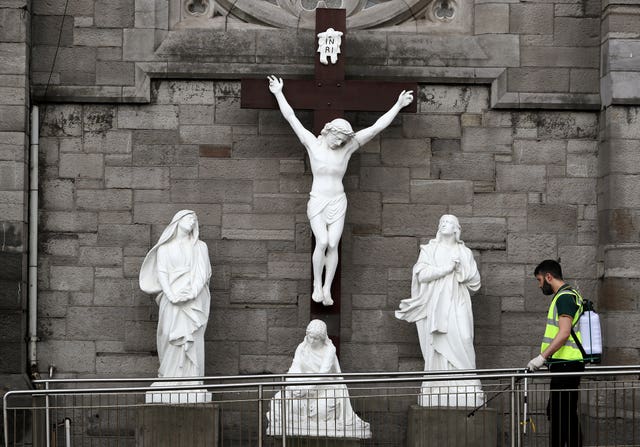 A man sprays disinfectant at a statue of the crucifixion of Jesus outside St Mary of the Angels church in Dublin, on Good Friday (Brian Lawless/PA)