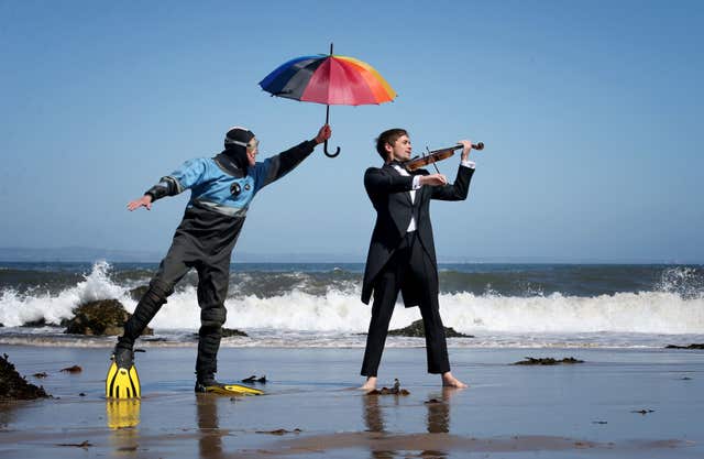 Calum Duncan of the Marine Conservation Society listens as Thoren Ferguson plays the Il Mare Violin which is made from driftwood (Jane Barlow/PA)