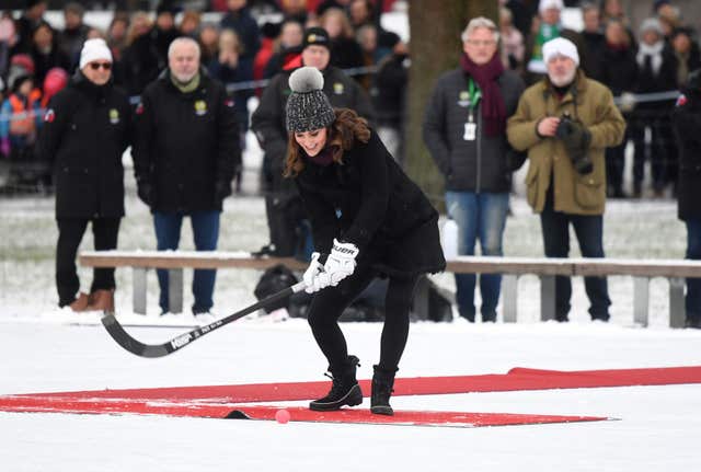 The Duchess of Cambridge hits a hockey ball as she and the Duke of Cambridge meet a group of local bandy hockey players