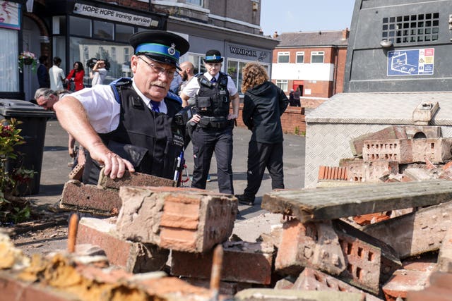 A police community support officer removes bricks from a damaged wall on Sussex Road in Southport 