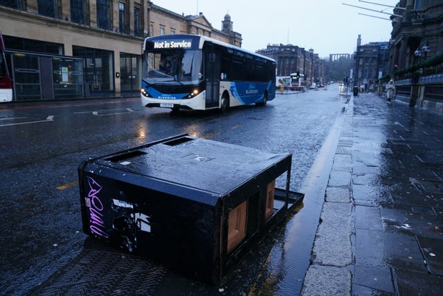 A fallen bin in the road and a bus reading 'not in service' drives around it 