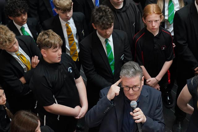 Pupils stand behind Sir Keir Starmer as he speaks into a microphone during a visit to a school in Northamptonshire