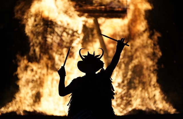 A man wearing a costume is in silhouette in front of a bonfire