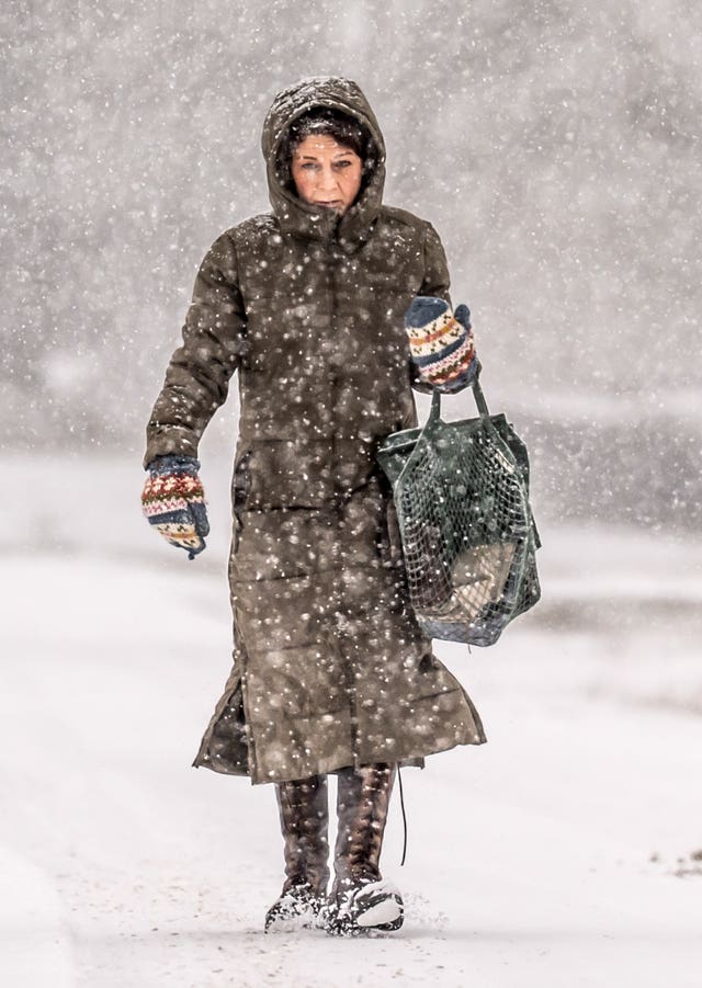 A woman dressed in a coat and gloves walking in the snow