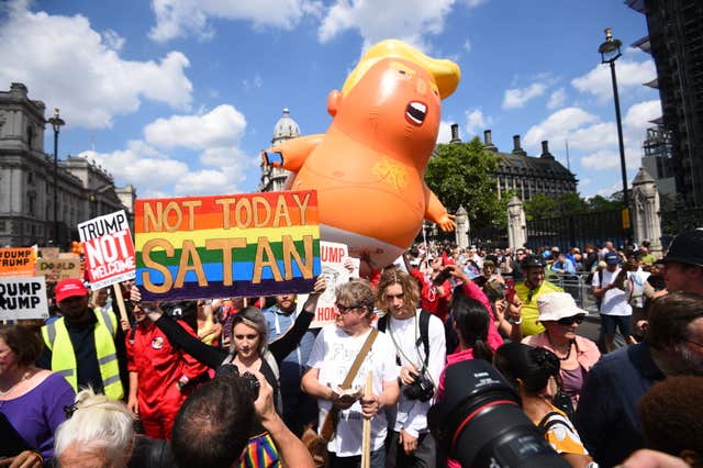 Trump Baby balloon seen in the background behind protesters including one carrying the sign 