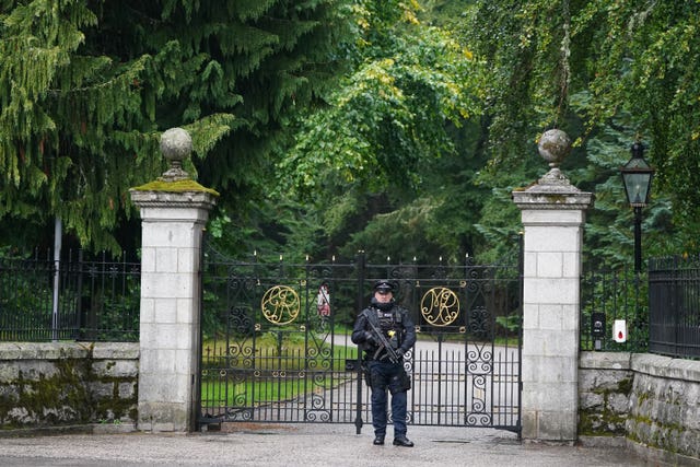 A uniformed armed police officer stands guard at the iron gates of Balmoral Castle