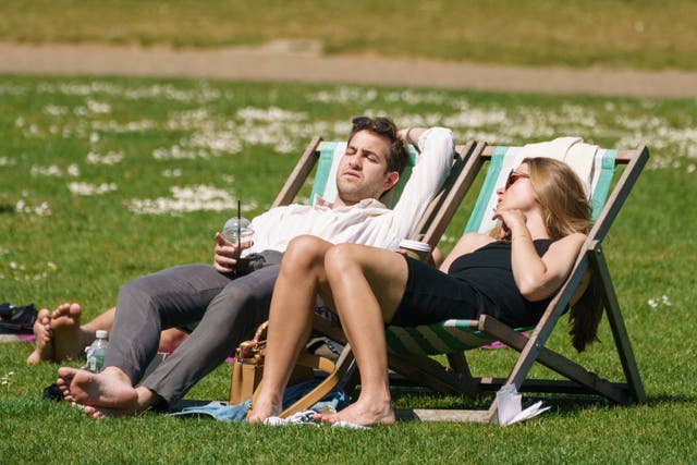 A man and woman relax on deckchairs on grass, in the sunshine