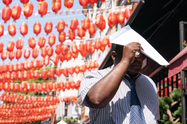 A man uses an envelope to shade himself from the sun in Chinatown, central London