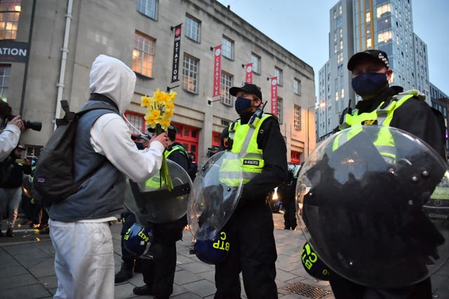 A man holds a bunch of daffodils in front of a police line near to Bridewell police station 