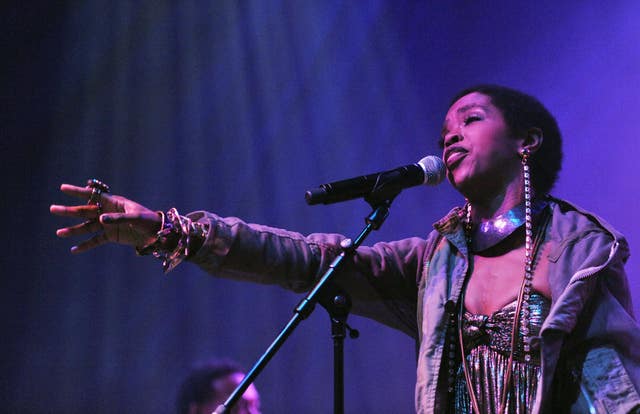 Lauryn Hill reaching out in front of her as she sings into a microphone