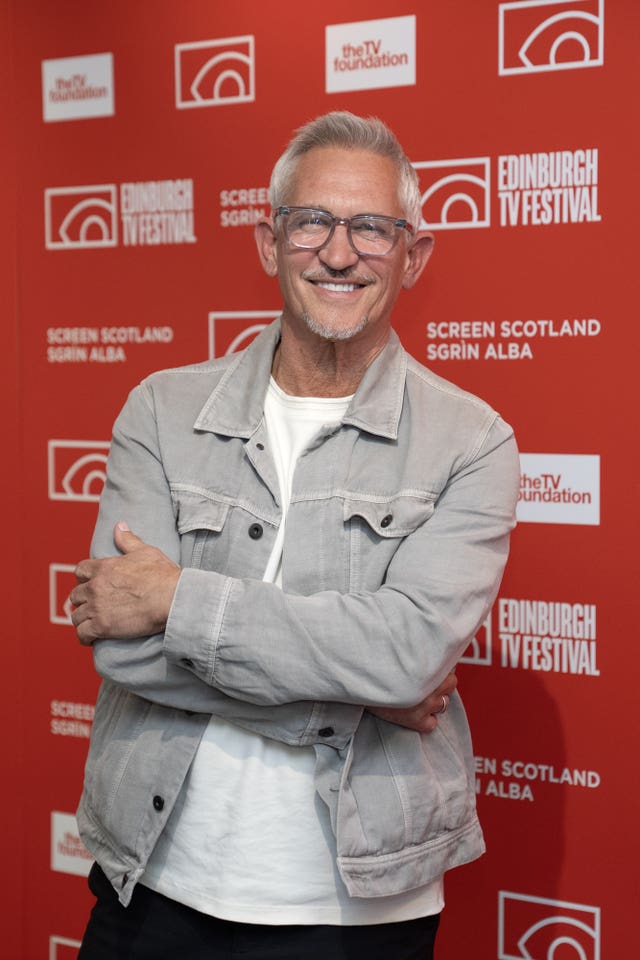 Gary Lineker wearing a white shirt and grey jacket smiling in front of a red banner promoting the Edinburgh TV Festival