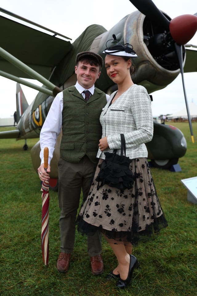 A couple dressed in period clothing pose in front of a plane