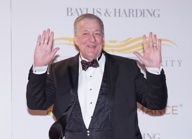 Sir Stephen Fry smiling while raising his hands in the air