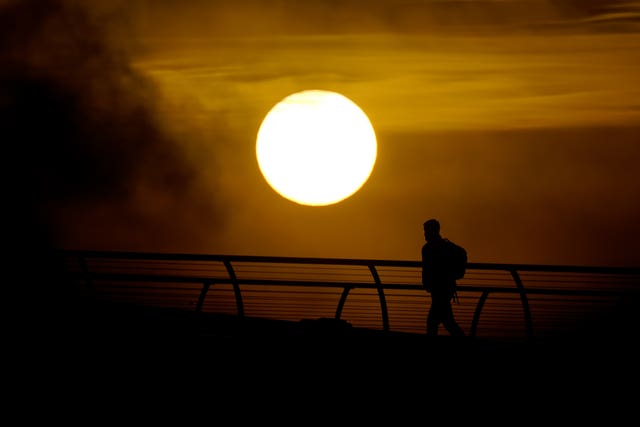 Sun low in the sky, behind the silhouette of a person walking across a bridge