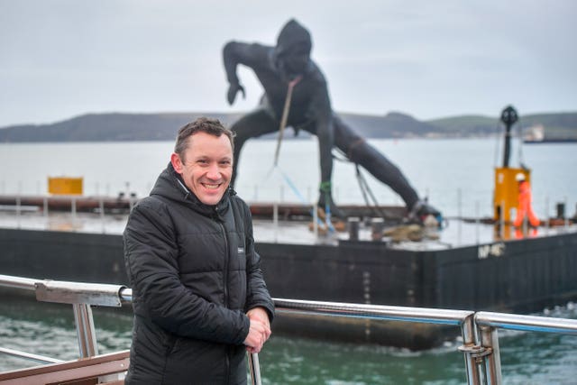 Artist Joseph Hillier on a boat beside his sculpture Messenger