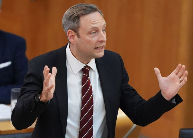 Liam Kerr gesturing with both arms while speaking in Holyrood