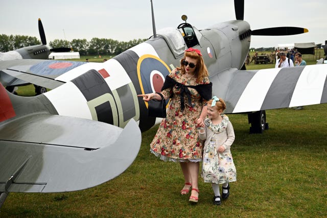 A woman holds a girl's hand as they take a closer look at a vintage plane