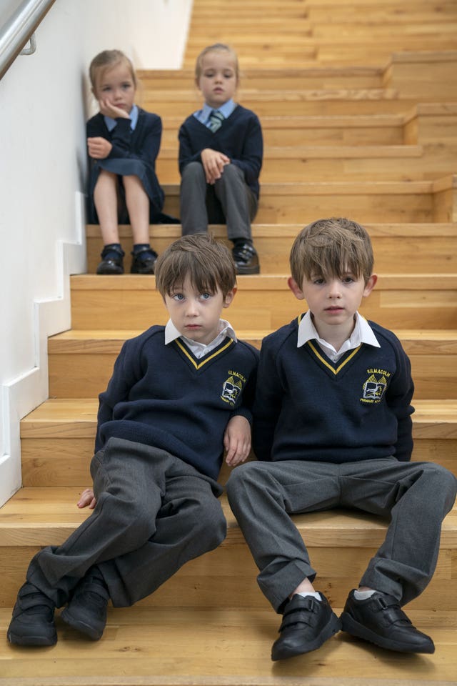 Twin girls sit on a step, with twin boys below them, all dressed in school uniform