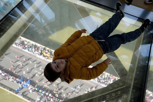 A child lies on the glass floor of Tower Bridge as runners cross underneath