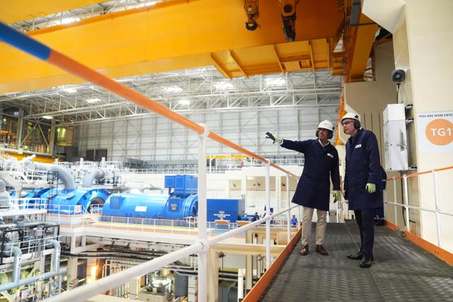 Rishi Sunak in white hard hat and ear defenders stands pointing with a worker in the turbine room at Sizewell B