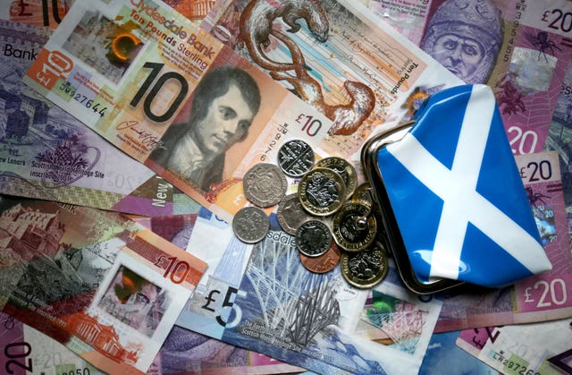 Saltire purse sitting on Scottish notes, with coins spilling out of it