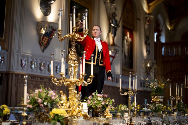 A member of Royal Household staff lights a candle during table preparations in St George’s Hall