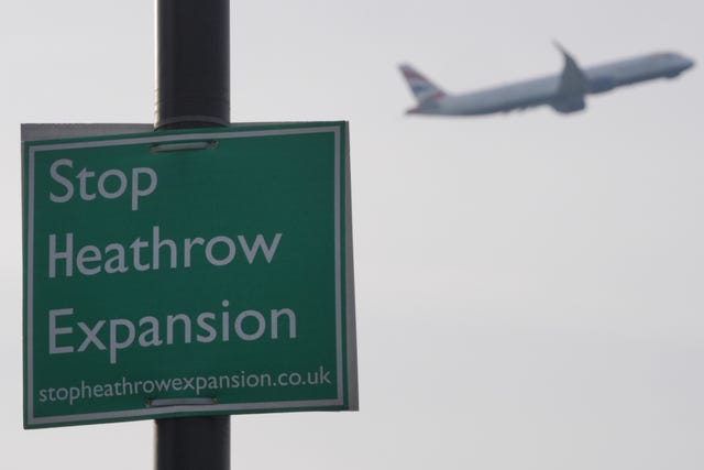 A plane flies past a 'Stop Heathrow Expansion' sign on a post
