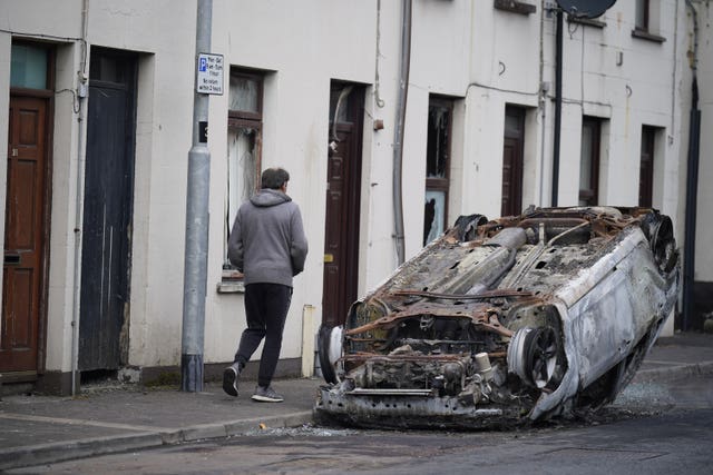 A man walks past a burnt-out overturned car on the street following a second night of violence in Ballymena 