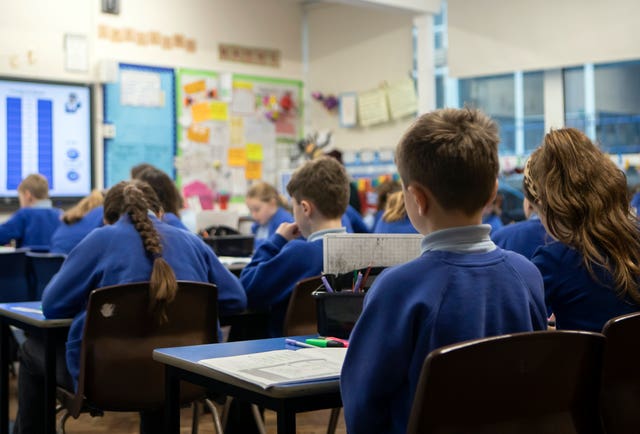 View of a school classroom, with pupils in blue jumpers seated with their backs to the camera
