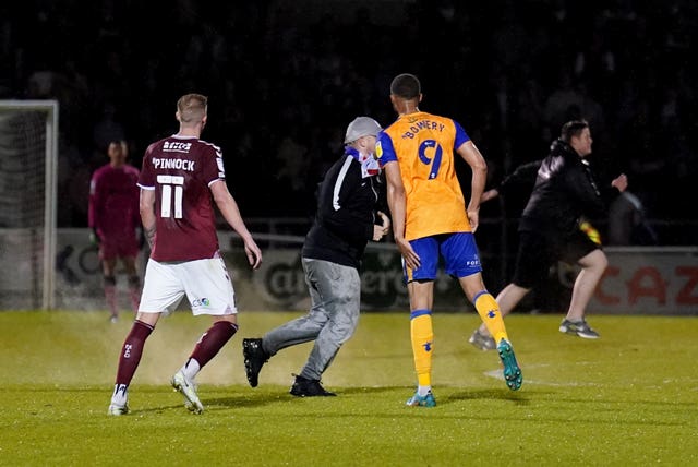 A pitch invader clashes with Mansfield's Jordan Bowery at Northampton earlier this week