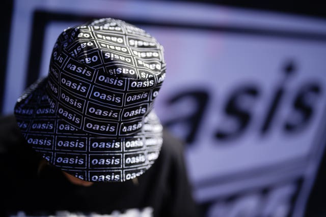 An Oasis fan wears a bucket hat with the band logo