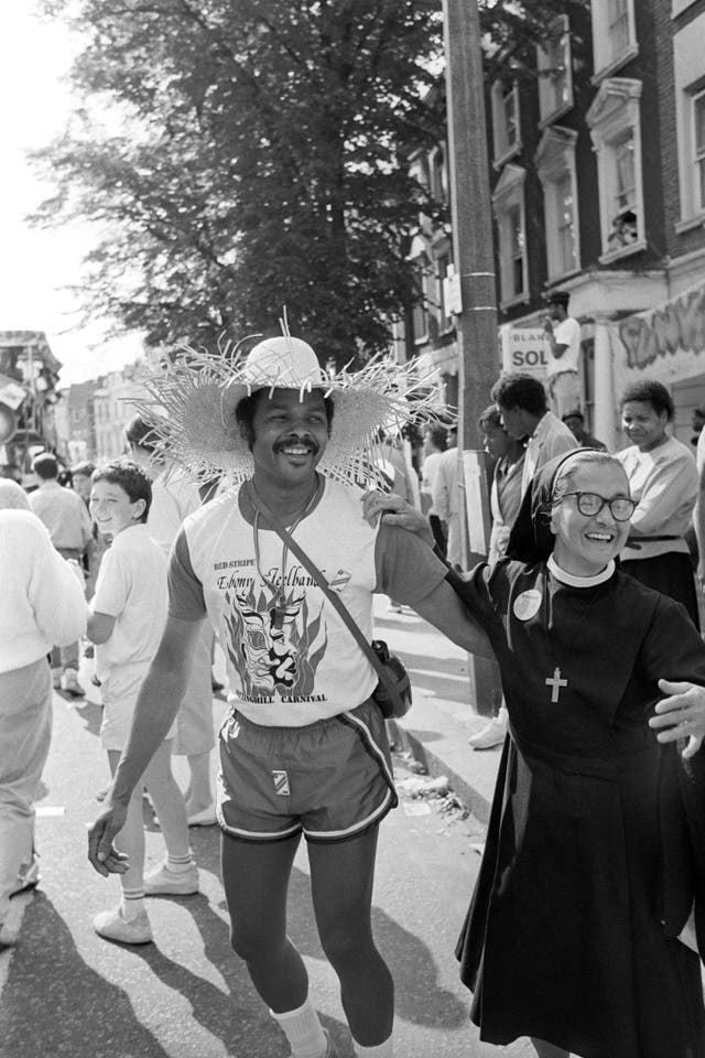 A nun enters into the carnival spirit by dancing in the street with a reveller from the Ebony Steel Band float at the Notting Hill Carnival in west London in 1986 (PA)