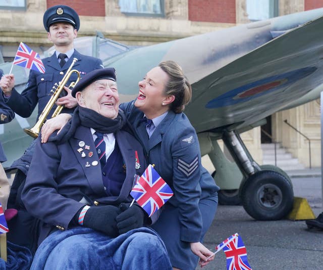 Henry Rice, 98, a Normandy veteran who served aboard HMS Eastway on VE Day, reacts to receiving a kiss from D-Day Darlings lead singer Katie Ashby during a photocall with a full-size replica Spitfire outside the Royal Albert Hall, London