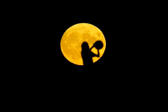 A person plays with a ball as the Sturgeon supermoon, the final supermoon of the year, rises over a hill in Ealing, west London 