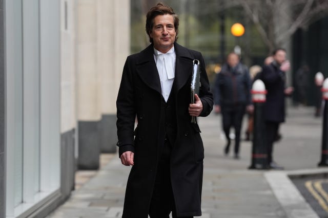 David Sherborne in a black coat and white shirt carries a binder as he walks down a street