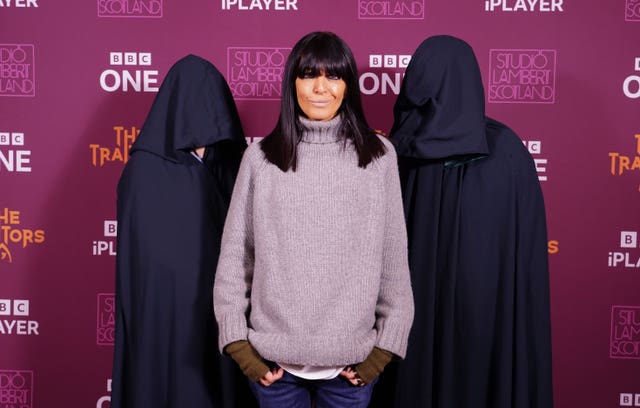 Claudia Winkleman flanked on either side by two hooded figures