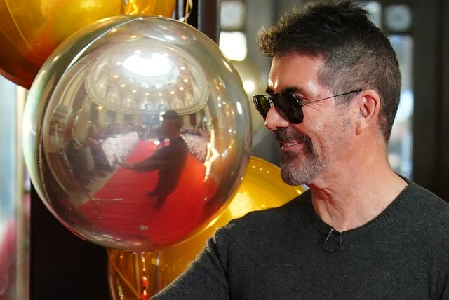 Simon Cowell next to a large yellow and silver balloons