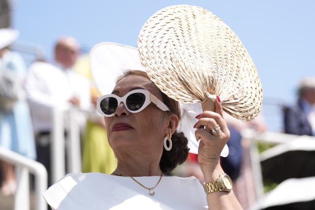A glamourous woman wearing white sunglasses uses a hand fan to cool herself down at Ascot Racecourse