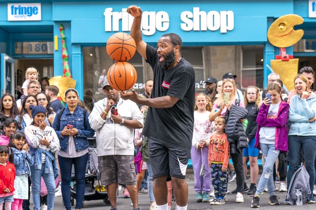 Man balancing two basketballs in front of Fringe shop in Edinburgh 