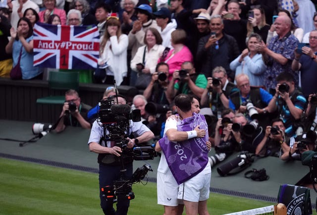 Andy Murray and Jamie Murray hug while fans wave flags in the crowd