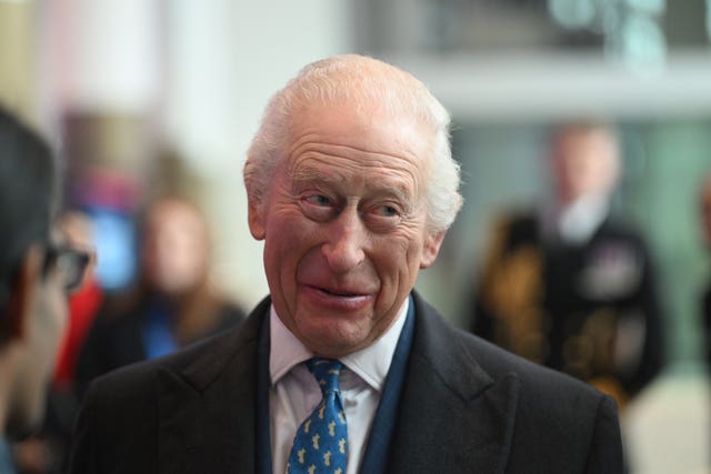 The King in a suit, tie and overcoat smiles during a visit to Tottenham Hotspur Stadium, north London